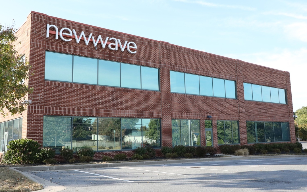Picture of the exterior of NewWave building, 2 story brick building with a lot of glass windows